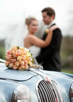 a bride and groom standing next to a blue car with flowers on the front hood