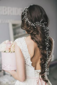 the back of a bride's dress holding a pink box with flowers on it