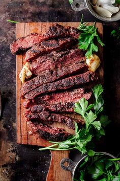 sliced steak on a cutting board with parsley next to it and two bowls of sauces