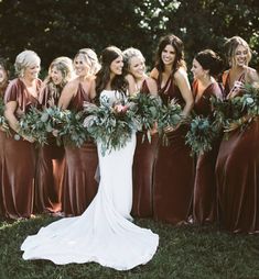 a group of women standing next to each other in front of green leaves and flowers