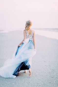 a woman in a blue dress walking on the beach with her back to the camera