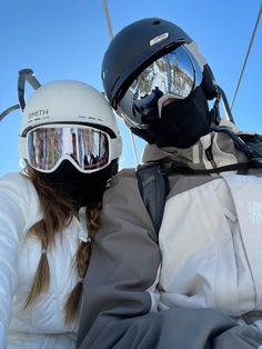 two people wearing helmets and goggles sitting on a ski lift with their arms around each other