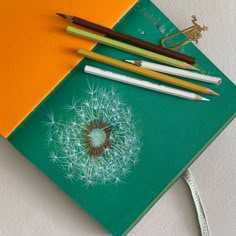 three pencils are laying next to each other on a piece of paper with a dandelion design