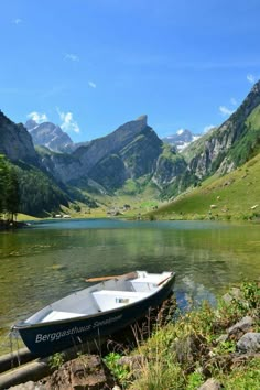 a small boat sitting on top of a lake next to a lush green mountain range