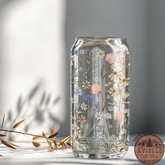 a glass vase with flowers painted on it and some plants next to it in front of a white wall