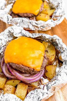 two hamburgers covered in cheese and onions sitting on tin foil over a wooden table