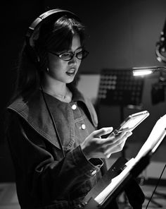 a woman wearing headphones is looking at her cell phone in the recording studio,