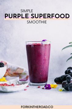 a purple smoothie in a glass next to berries and blueberries on a plate