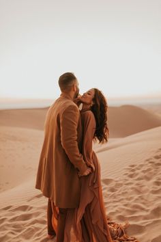 a man and woman standing in the sand with their arms around each other as they kiss