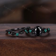 two black rings with green stones are on top of a wooden table and one is in the middle