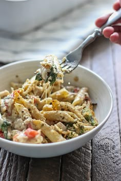 a person is holding a fork full of pasta and broccoli in a white bowl