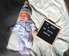 a baby doll is posed next to a sign that says it's been a one - year - old month