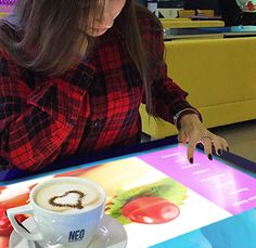 a woman sitting at a table with a cup of coffee in front of her and an advertisement on the table