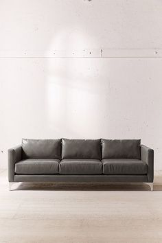 a black leather couch sitting on top of a hard wood floor next to a white wall