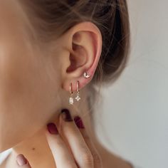 This stacking set features 3 different earrings, all made from 18 karat gold-plated sterling silver. It has: ✅ One small huggie hoop earring with a single, clear-coloured, Baguette-cut zircon stone in a four-prong setting hanging from its lower edge;  ✅ One small huggie hoop earring with a small flower-shaped pendant, which is decorated with four round, clear-coloured zircon stones, and  ✅ One small stud earring with two clear-coloured, oval-shaped zircon stones arranged in a V-shape, with a but Different Earrings, Earring Stack, Stacked Earrings, Ear Stack, Hoop Earring Sets, Small Earrings Studs, Ear Piercing, Delicate Earrings, Baguette Cut