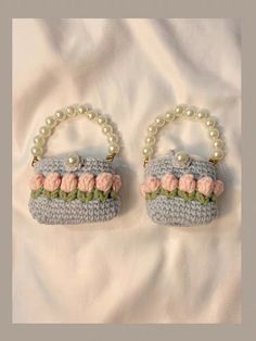 two crocheted purses with flowers and pearls hanging from them on a white sheet