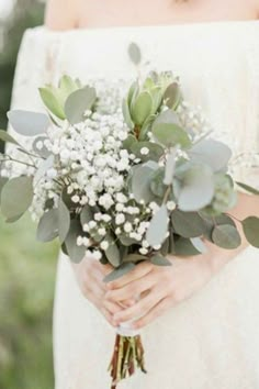 a woman holding a bouquet of flowers and greenery in her hands while wearing an off the shoulder dress