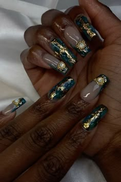 a woman's hands with gold and green nail polishes on their nails, holding onto her manicures