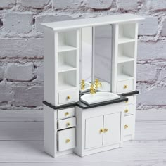 a white wooden cabinet with drawers and gold accents on the top, next to a brick wall