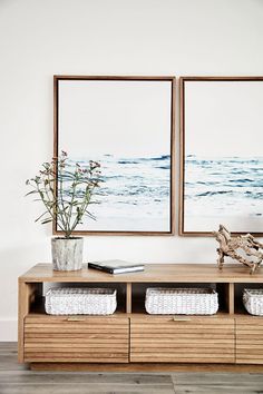 two framed pictures hang on the wall above a wooden table with baskets and vases