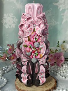 a pink and black candle holder sitting on top of a wooden stump next to flowers