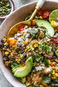 a bowl filled with salad and topped with avocado, tomatoes, black beans, cilantro, lime wedges