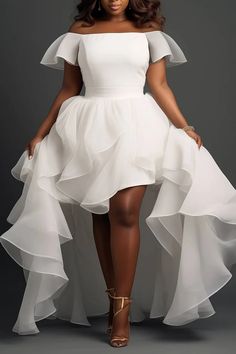 a woman wearing a white dress with ruffled layers on the skirt and heels, standing in front of a gray background