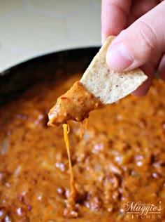 a hand holding a tortilla chip and dipping it into a chili cheese dip