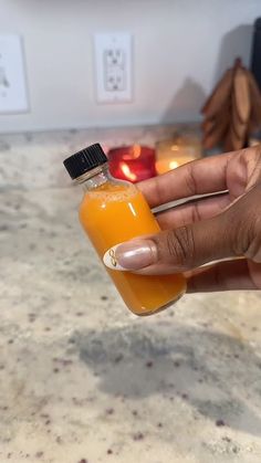 a person holding a bottle of orange juice in front of some candles on a counter