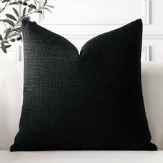 a black pillow sitting on top of a white couch next to a potted plant