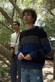 two young men standing next to each other in the woods