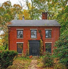 an old red brick house with black door and windows in the fall leaves on the ground