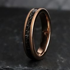 a wedding ring with black diamonds on it sitting on top of a stone slabd surface