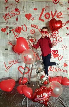 a young boy is standing on a ladder with balloons and heart shaped balloons in front of him