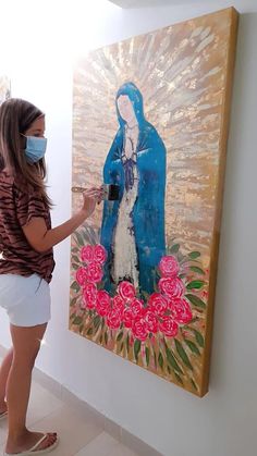 a woman wearing a face mask paints a painting on a wall with flowers in front of her