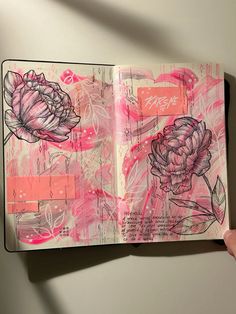 a hand holding up an open notebook with flowers on the pages and writing in pink ink