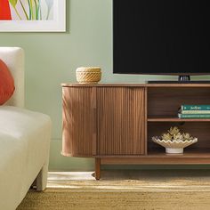 a flat screen tv sitting on top of a wooden entertainment center next to a white couch