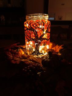 a jar filled with lights sitting on top of a leaf covered table next to a tree