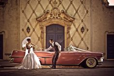 a bride and groom standing in front of an old fashioned red car with the door open