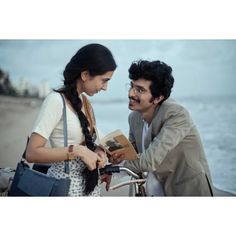 a man and woman standing next to each other on the beach with a bike in front of them