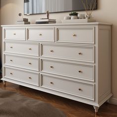 a white dresser with gold handles and drawers in front of a large mirror on the wall