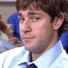 a man in a blue shirt and tie looking off to the side with other people behind him