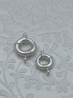 two pairs of silver colored metal hoop earrings on a white background with floral design pattern