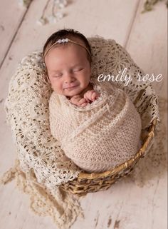 a newborn baby is wrapped in a white wrap and laying on top of a wicker basket