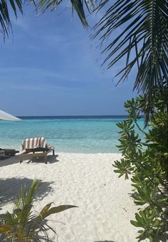 an umbrella and lounge chair on the beach with clear blue water in the back ground