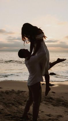 a man carrying a woman on his back while standing in front of the ocean at sunset