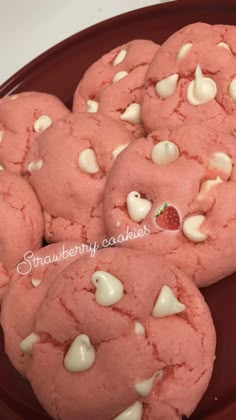 some pink cookies with white chocolate chips on a red plate and one has a strawberry