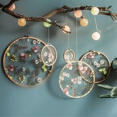 three plates hanging from a branch with flowers on them and some lights in the background