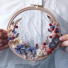 a woman holding a hoop with flowers on it in front of her face while wearing a white dress