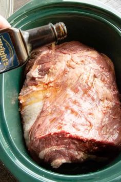 a person is pouring seasoning into a piece of meat in a green bowl